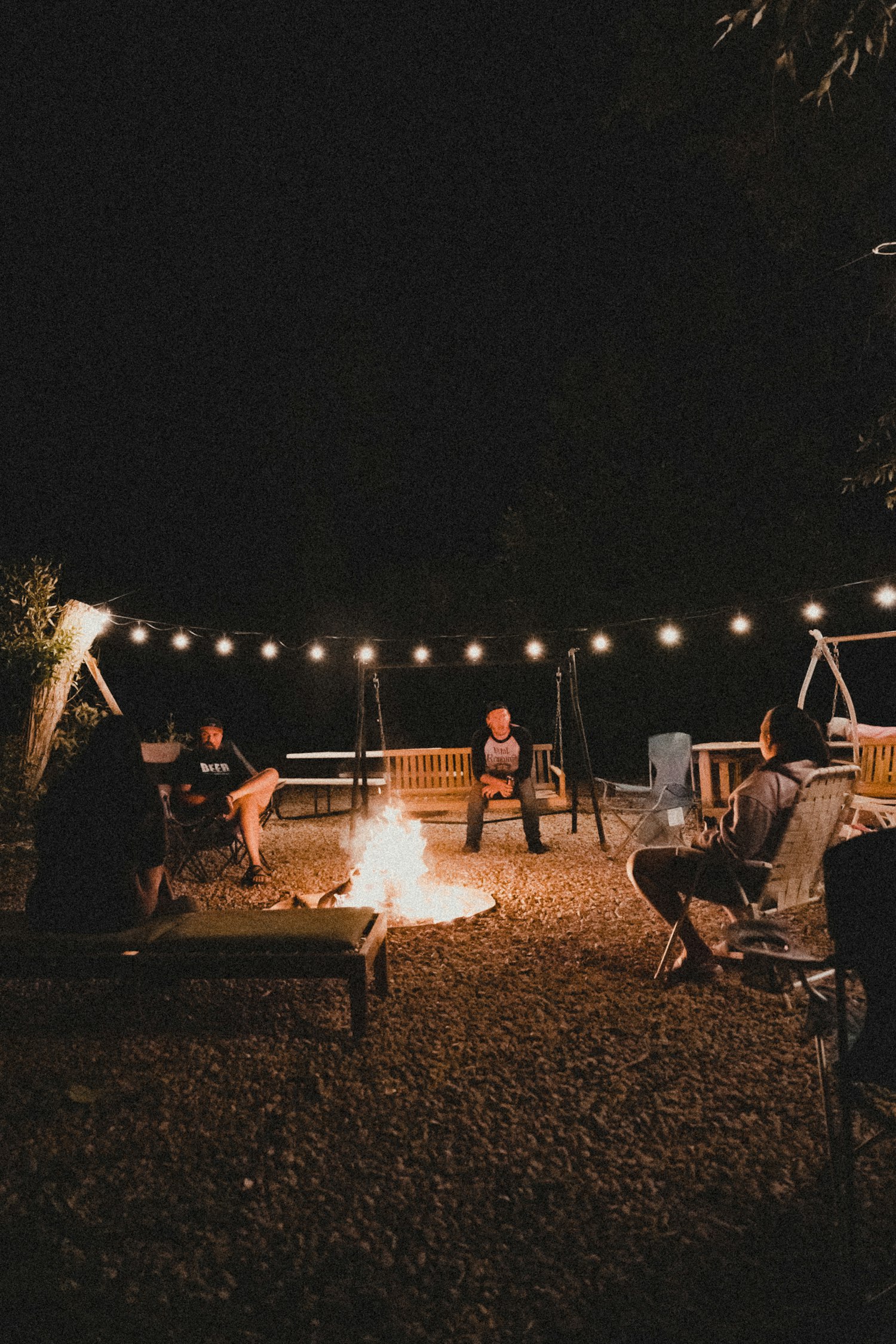 Friends gathered around a campfire under string lights