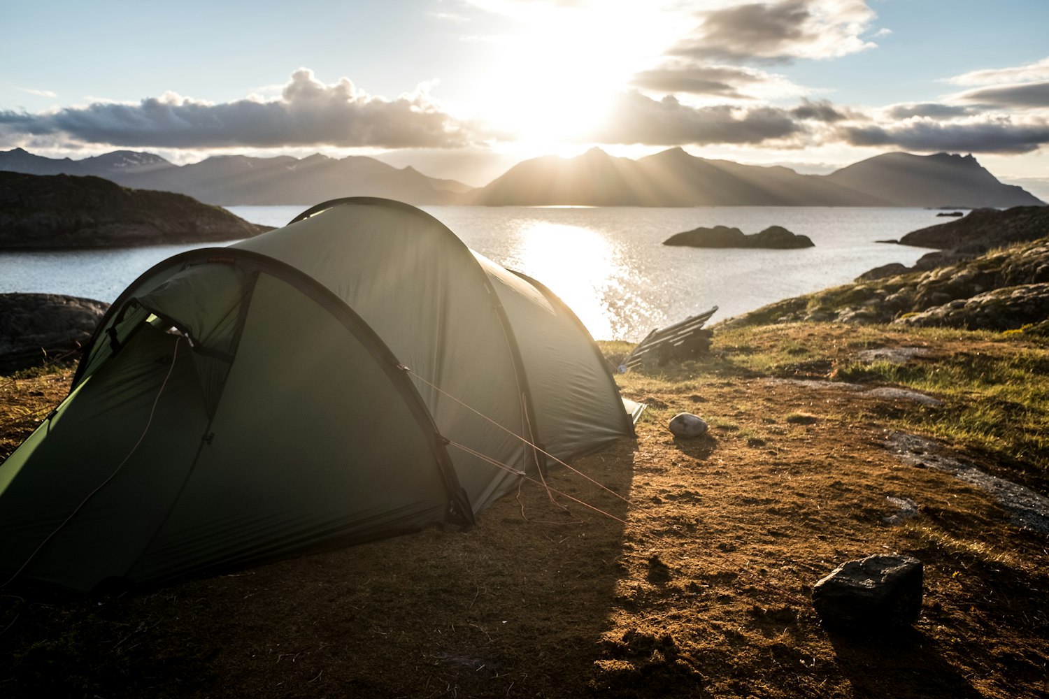 A tent pitched on a ridge overlooking a mountain lake at golden hour